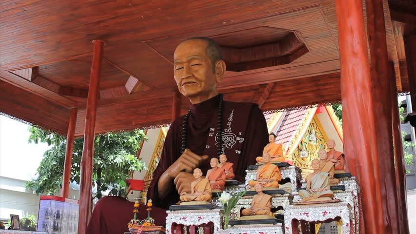 An oversized Buddhist monk statue sits amongst several smaller statues at a temple in Bangkok, Thailand.