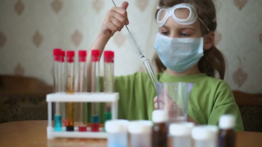 Little girl in face mask cleans chemical test tube by brush