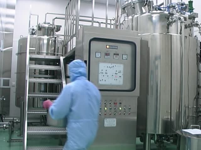 A technician pouring liquid medicine to a mixing machine in a pharmaceutical manufacturing factory.