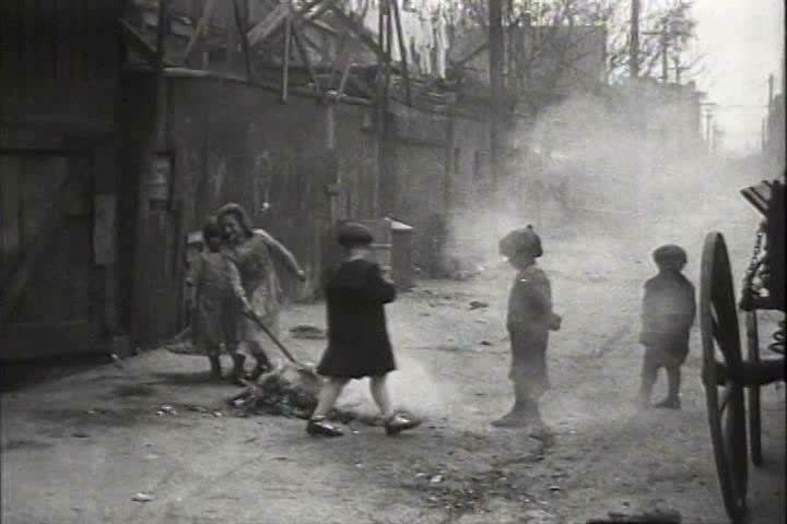 1910s, 1920s - Children play with a smoking pile of rubbish in an alley