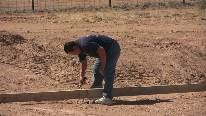 A hispanic man removing a steel stake while working on forms for a new home foundation.