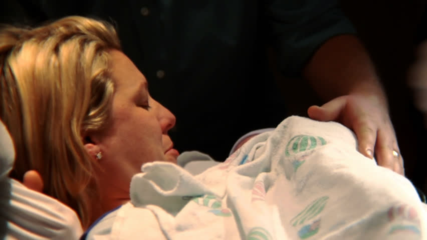 Newborn baby being held up and handed to its mother.