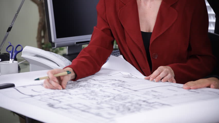 Office scene of an architect and his associates reviewing a set of building plans.