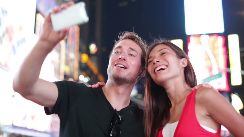 Dating young couple happy in love taking self-portrait photo on Times Square, New York City at night. Beautiful young multiracial tourists having fun date, Manhattan, USA. Asian woman, Caucasian man.