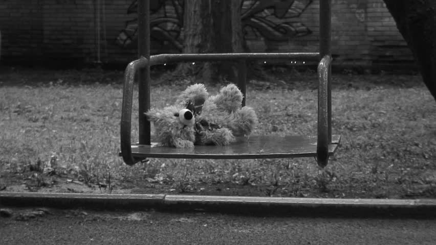 Forgotten Teddy bear on a swing under rain. Deep depression theme. Black and white.