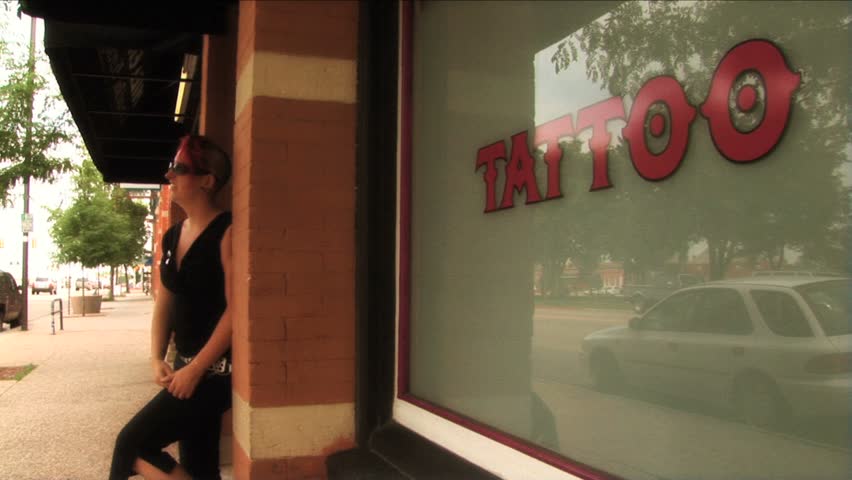 (1112) Tattooed young woman with Mohawk in front of Tattoo Parlor. Good for themes of youth culture and fashions, relationships and emotions.