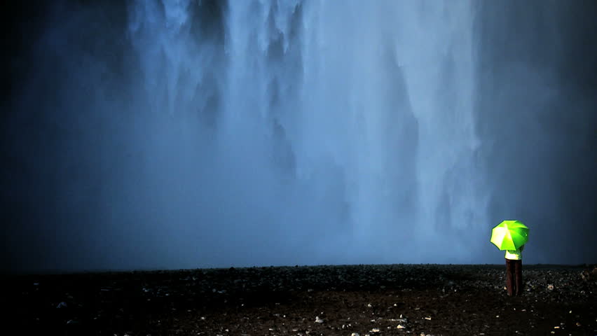 Concept shot of lone female standing on the edge of a waterfall with green umbrella to shelter from climate change 60 FPS