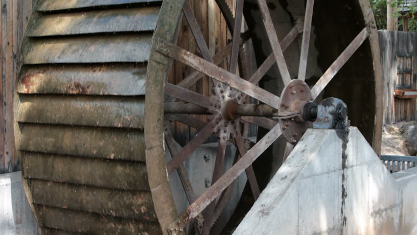 Old antique water wheel turning against a wood building. Steel wheel and spokes close. Turning from power of a small creek in central Utah. Used for a mill.