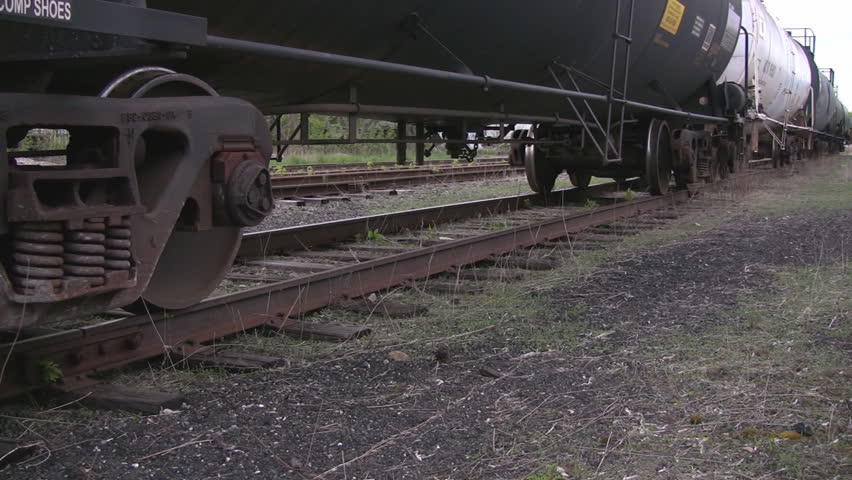 A pan along the train tracks at wheel level, showing a lineup of tankers, ending at the wheel assembly.