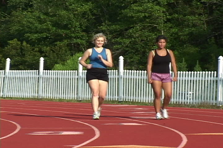 Two coeds power walk around the university track to exercise and loose weight.