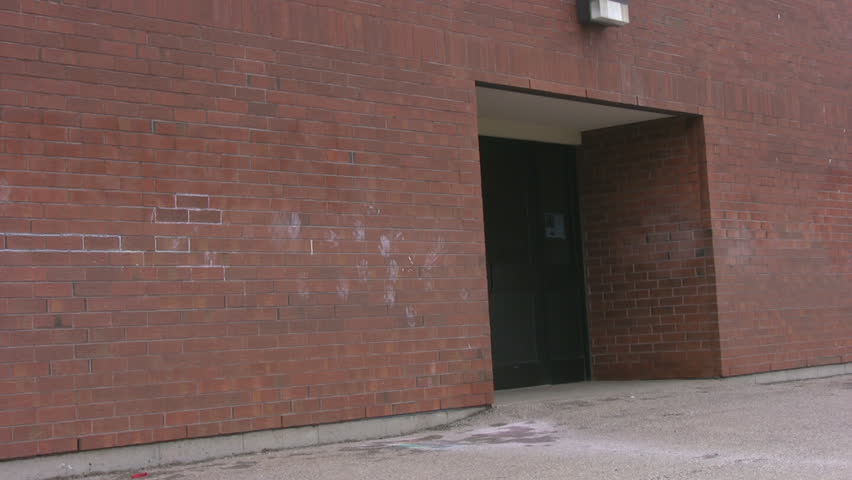 A pan of a rear entrance and along the red brick building of a public school.
