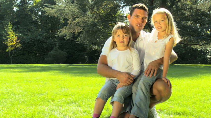 Young father tenderly holding his daughters while outdoors on a summers day