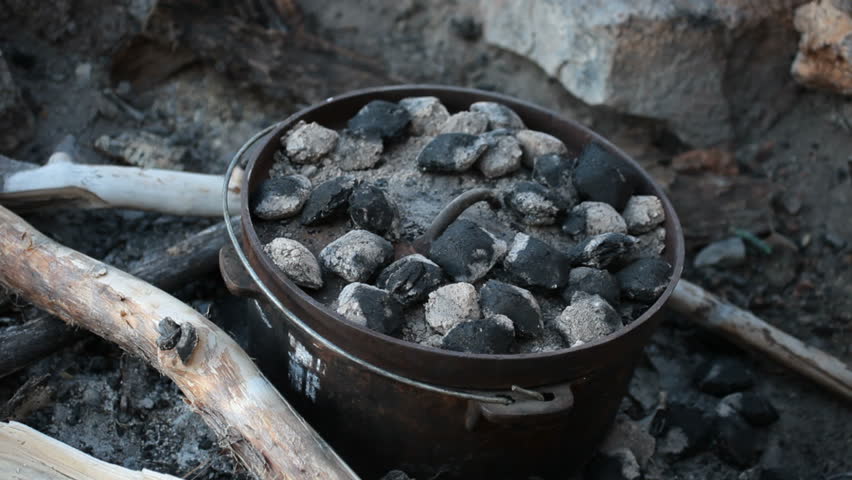 Dutch oven cooking over a camp fire outdoors. Lifting the lid with the claws of a hammer. Golden brown rolls cooking. Charcoal briquettes and fire heating the cast iron pot. Yummy food.