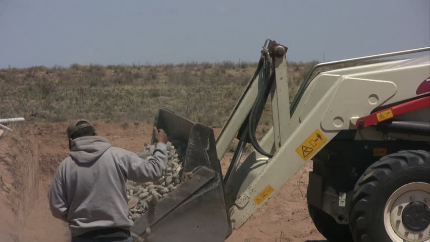 Man giving hand signals while rocks fall from backhoe bucket.
