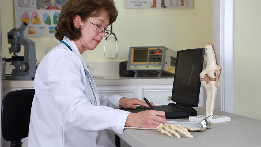 A female physician sitting at a desk in a medical clinic using a laptop to do take care of her record keeping.
