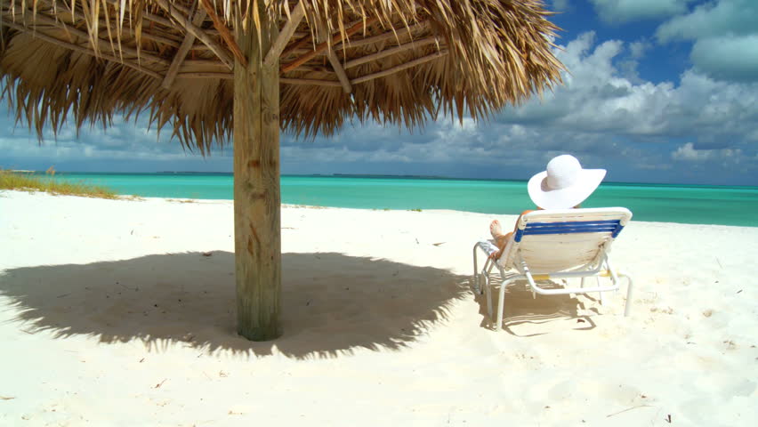 Elegant young female relaxing on white sandy beach looking at aquamarine waters