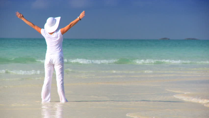 Elegant young female celebrating on a beautiful white sandy beach looking at aquamarine waters 60 FPS