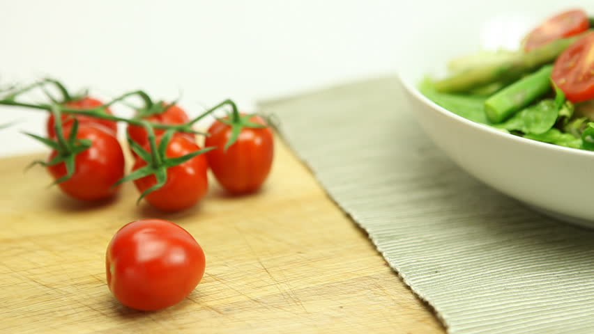 A fresh vine tomato is sliced and placed in a bowl of lush green salad