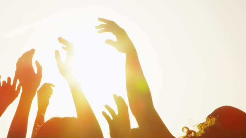 Happy carefree young group of friends having fun and dancing on the beach as the sun begins to set. In slow motion.