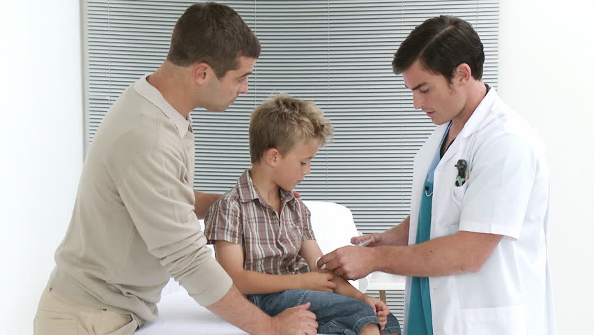 Footage in high definition of attractive male doctor giving an injection to a little boy who is with hid father in the medical office