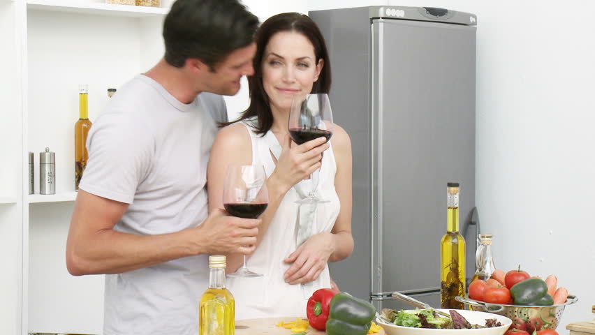 Happy couple drinking wine and eating salad in the kitchen at home. Footage in high definition