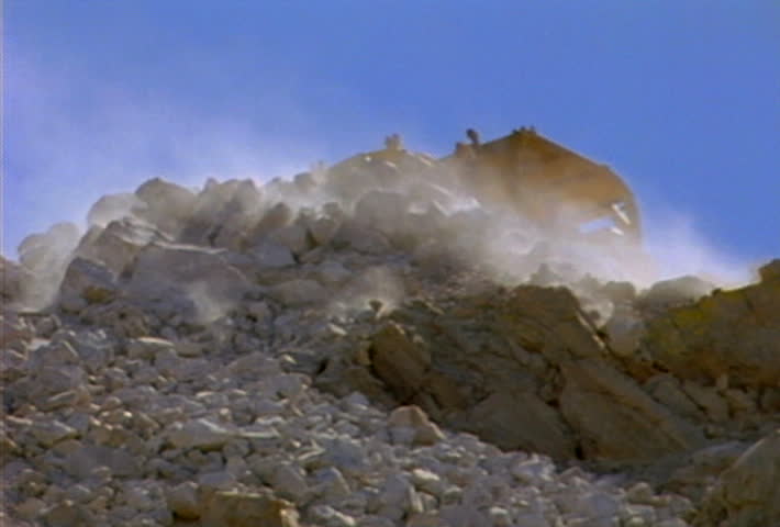 Boulders and smaller rocks roll and slide down a hill during a landslide.
