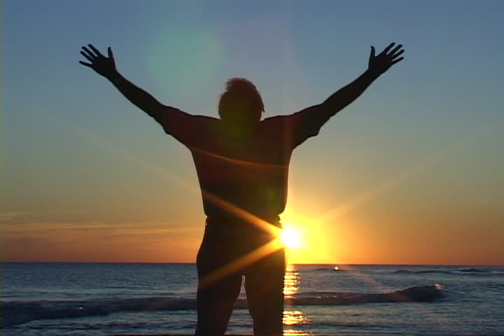 Mature man with hands raised, rejoices in prayer and worship at sunset on the beach. Shot on miniDV from a tripod.