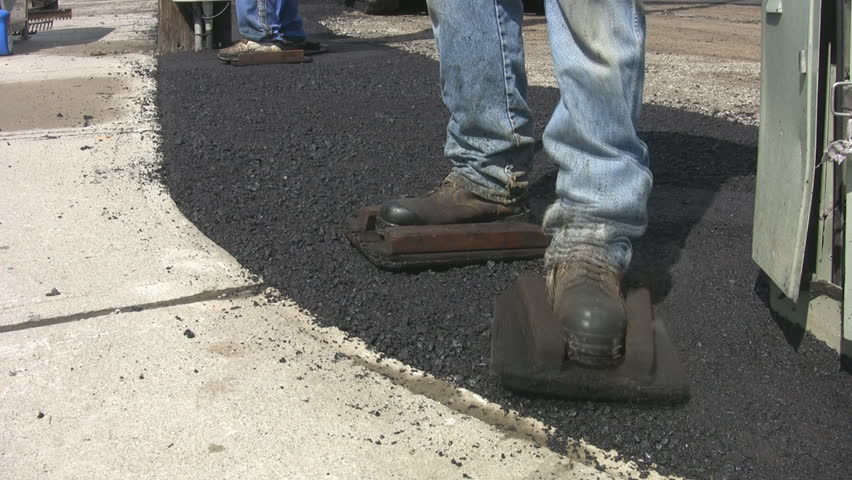 Men wear wooden frames over their workboots to flatten hot asphalt. Two shots.