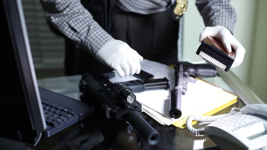 A man using a handheld light panel to examine weapons and other objects from a crime scene.