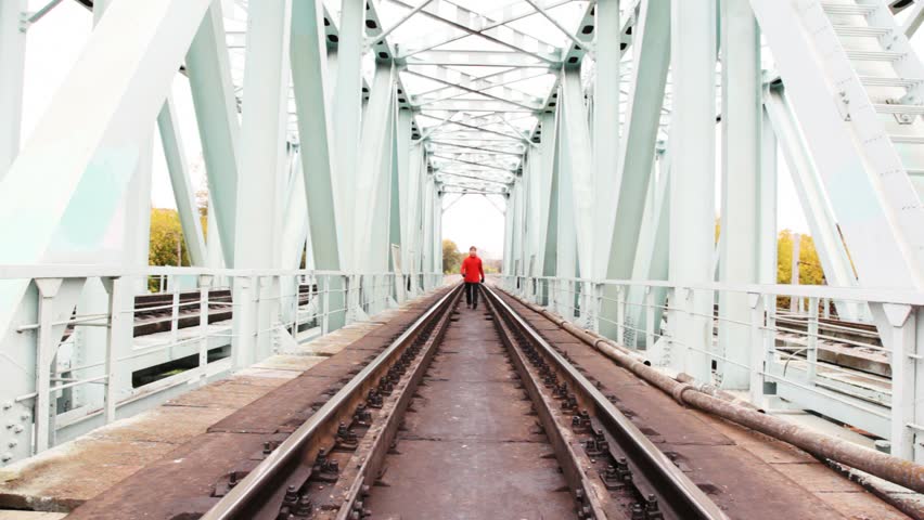 red-haired young man goes forward on camera on railway bridge 