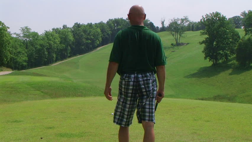 Golfer getting into stance and teeing off with driver onto fairway. 