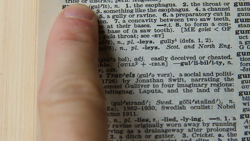 Close shot of someone looking up 'gullible' in the dictionary
