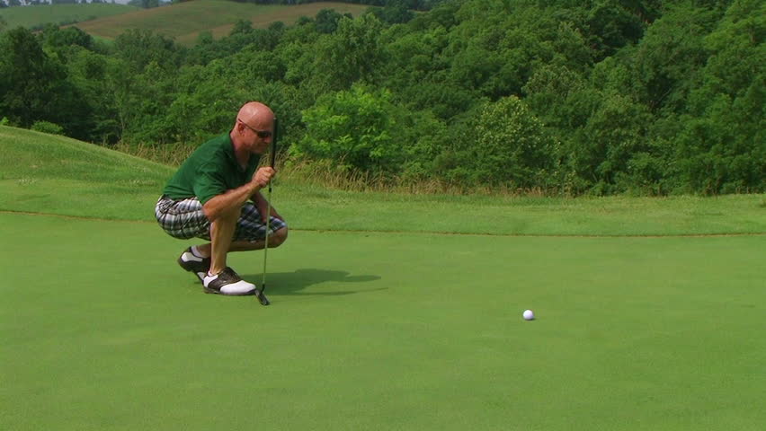 Golfer using putter to sink putt into hole. 