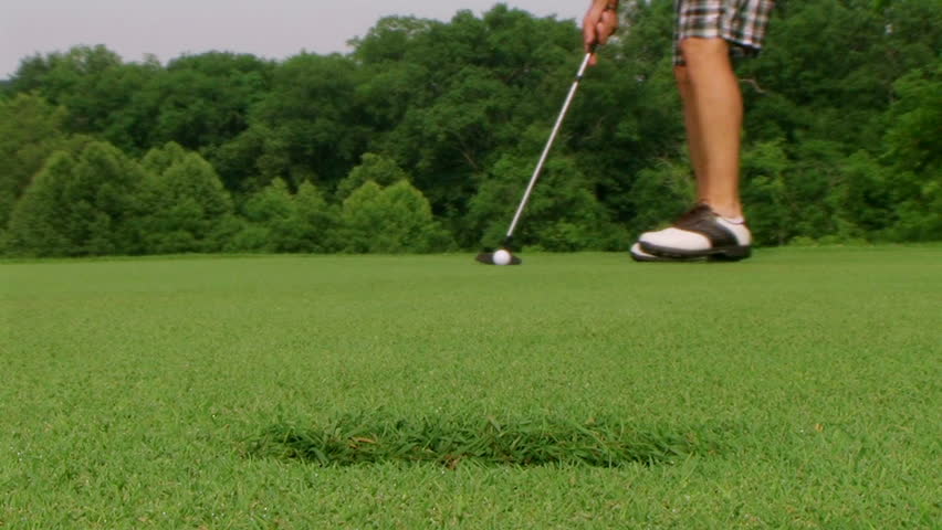 Close-up of golfer sinking long putt into hole. 