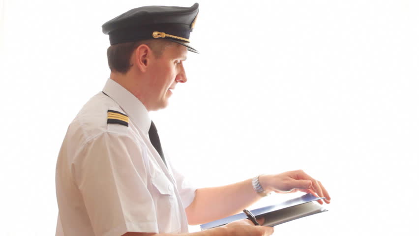 Airline pilot wearing hat, shirt with epaulets and tie filling in and checking papers flight plan, log book and weather forecast.
