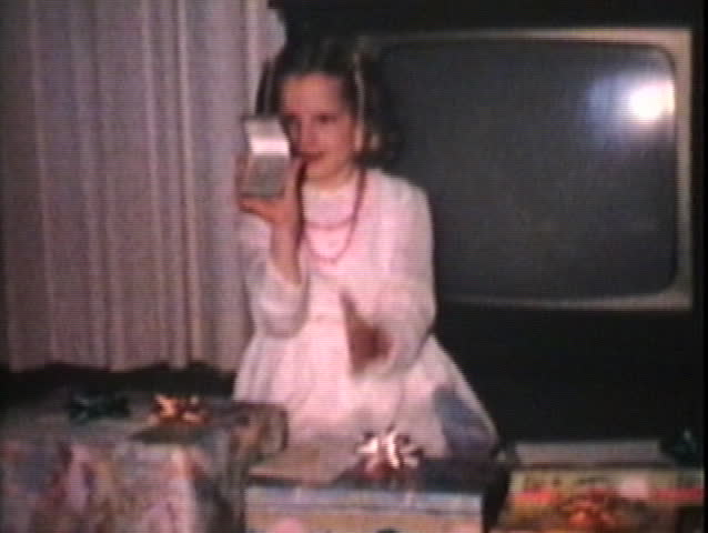Two adorable blond sisters open their Christmas presents in the living room in front of the old television. 