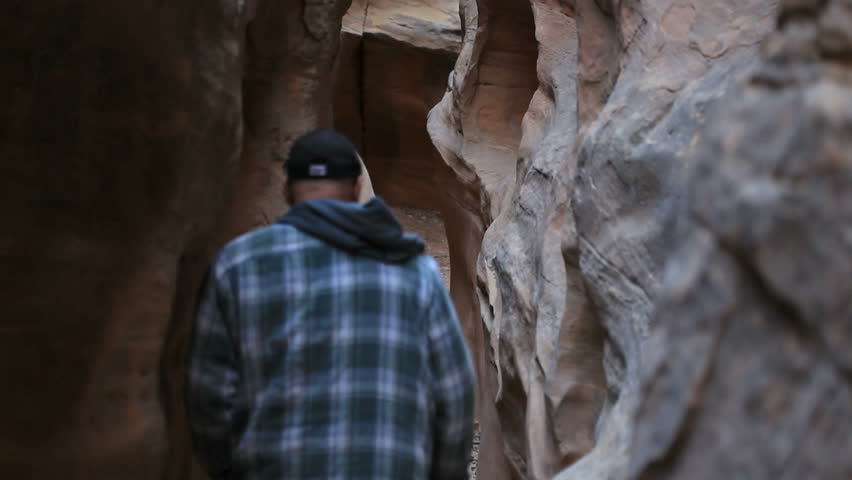 Man hiking and walking into a narrow slot canyon. Formed by rain and wind, a narrow opening in sheer sandstone cliff and mountain.