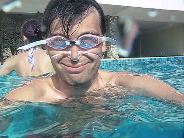 smiling young man in goggles diving into outdoor water pool 