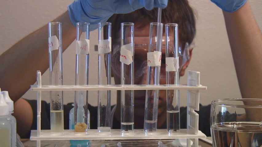 Chemistry student with gloves and goggles performs experiment with chemicals in beakers - HD 