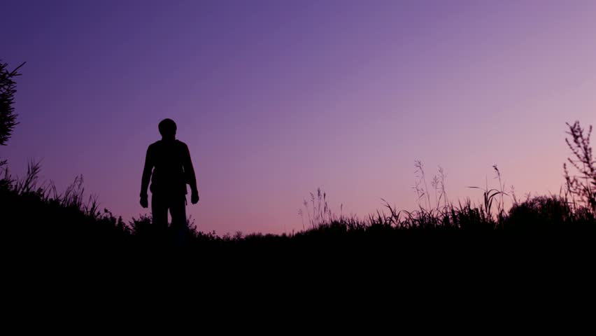 traveller with rucksack walks from camera against sunset summer sky 
