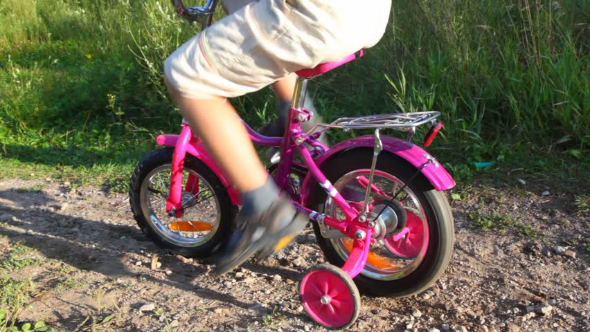 boy pedaling on bicycle in summer park, little girl pushes him 
