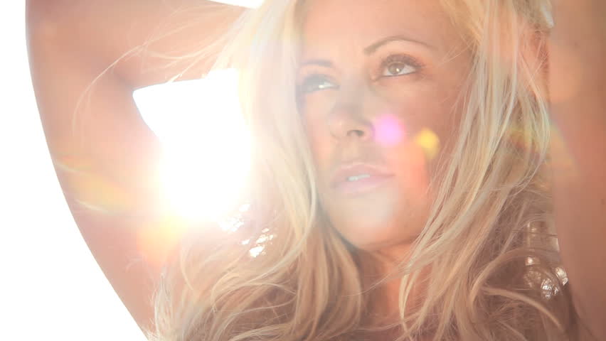Portrait of sensual blonde female with windswept hair & sun shining behind