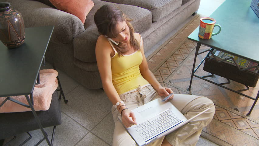 Young woman talking on cell phone while using laptop to purchase something online