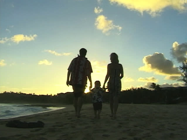 Family taking a sunset stroll on a sandy beach in Hawaii