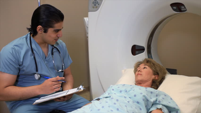 A technician asking a patient questions and filling out paperwork before a cat scan.