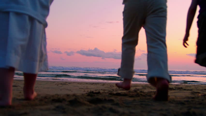 Three children and two adults run toward toward the sunset and jump on the beach. 