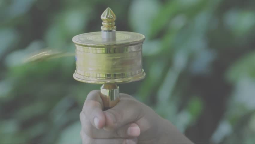 A pious tibetan man rotates a golden lection wheel.  