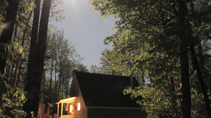 Timelapse of house in forest with stars and moon moving overhead