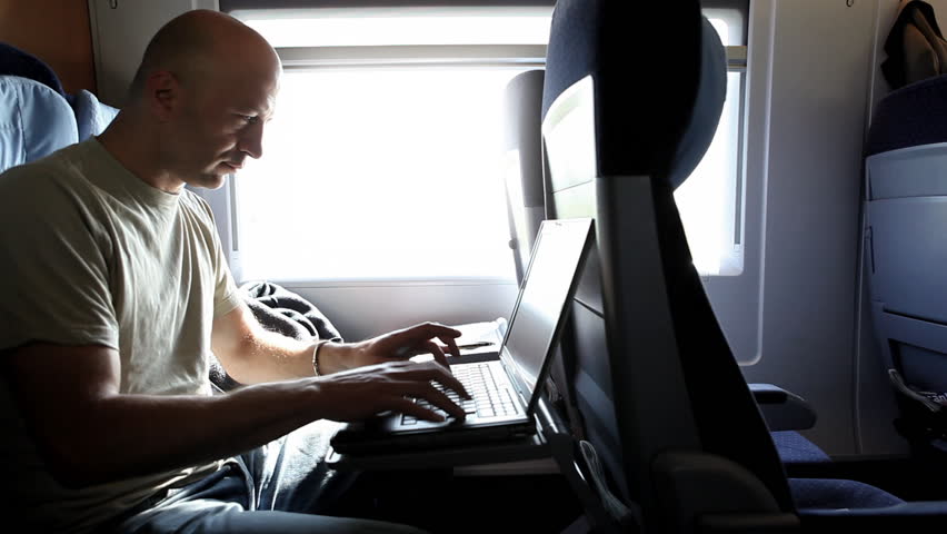 A middle-aged man is working with a laptop during a train ride, nice light effects by sunlight from a big window he is next to 