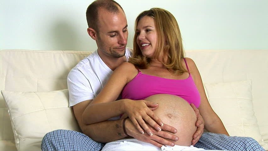 Pregnant couple sitting on couch caressing stomach